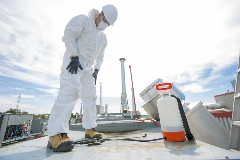 Two hood cleaning technicians working at a rooftop exhaust fan on a flat commercial roof