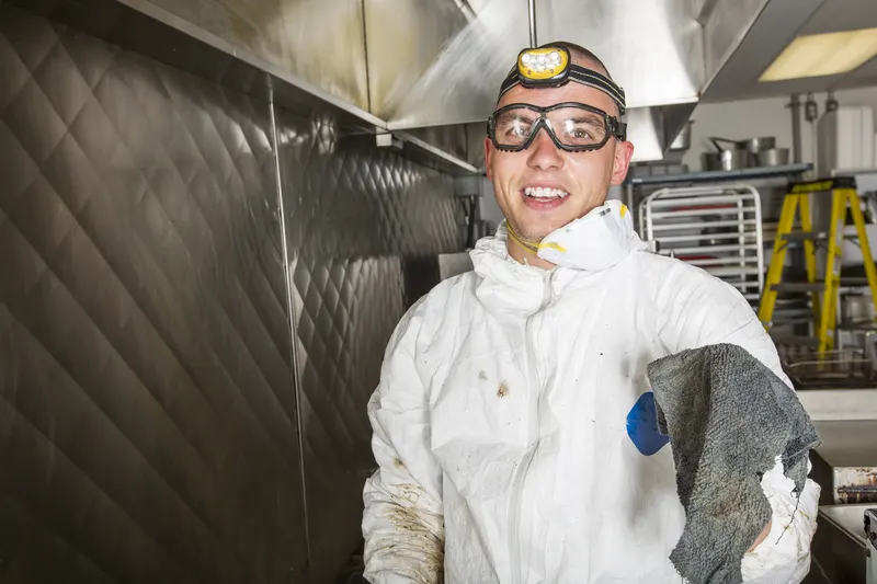 Hood cleaning technician holding a cleaning cloth in a restaurant kitchen with storage racks behind