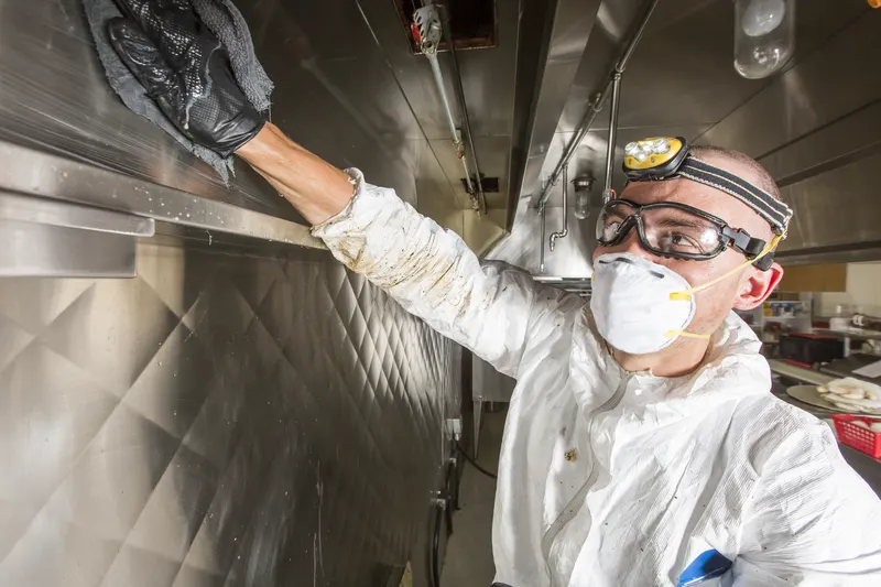 Technician reaching up to wipe a ledge inside a commercial kitchen exhaust plenum