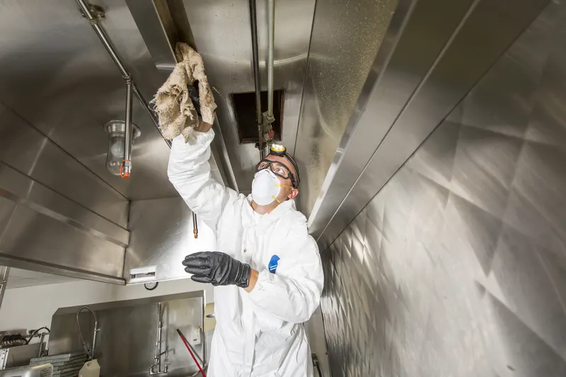 Technician wiping the plenum ceiling above the filter bank inside a commercial exhaust hood