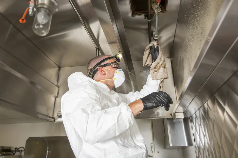 Technician wiping the lower edge of a stainless steel exhaust canopy beside the hood light